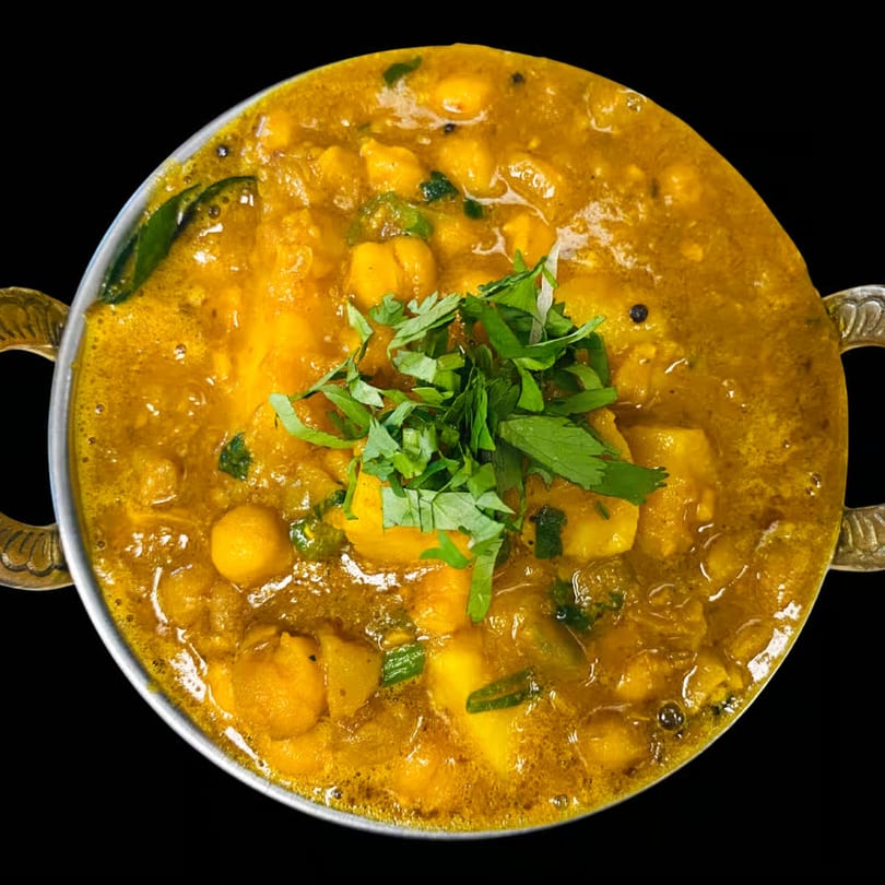 Dhaba Kitchen's Indian chickpea and potato curry, garnished with fresh cilantro, in a metal bowl.