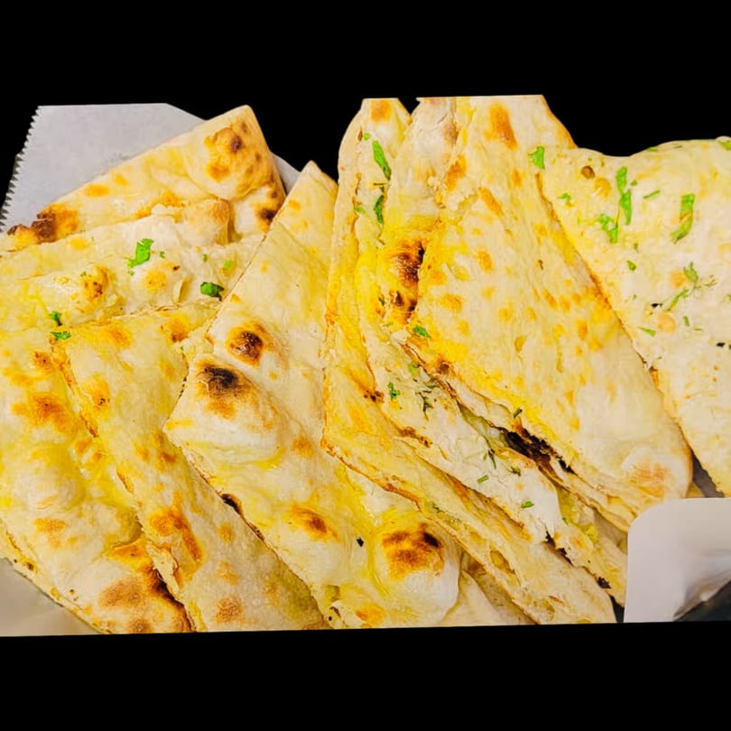 Close-up of Dhaba Kitchen's Indian naan bread, golden brown with green herbs, in a white basket.