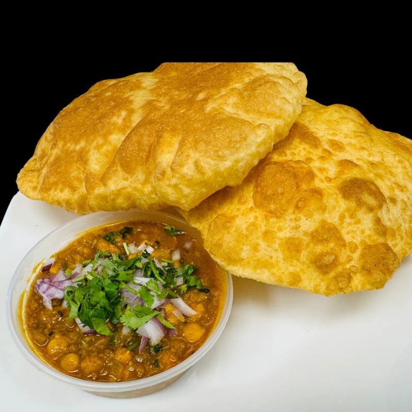 Two golden-brown Dhaba Kitchen puri breads next to a bowl of chana masala with onions and cilantro.