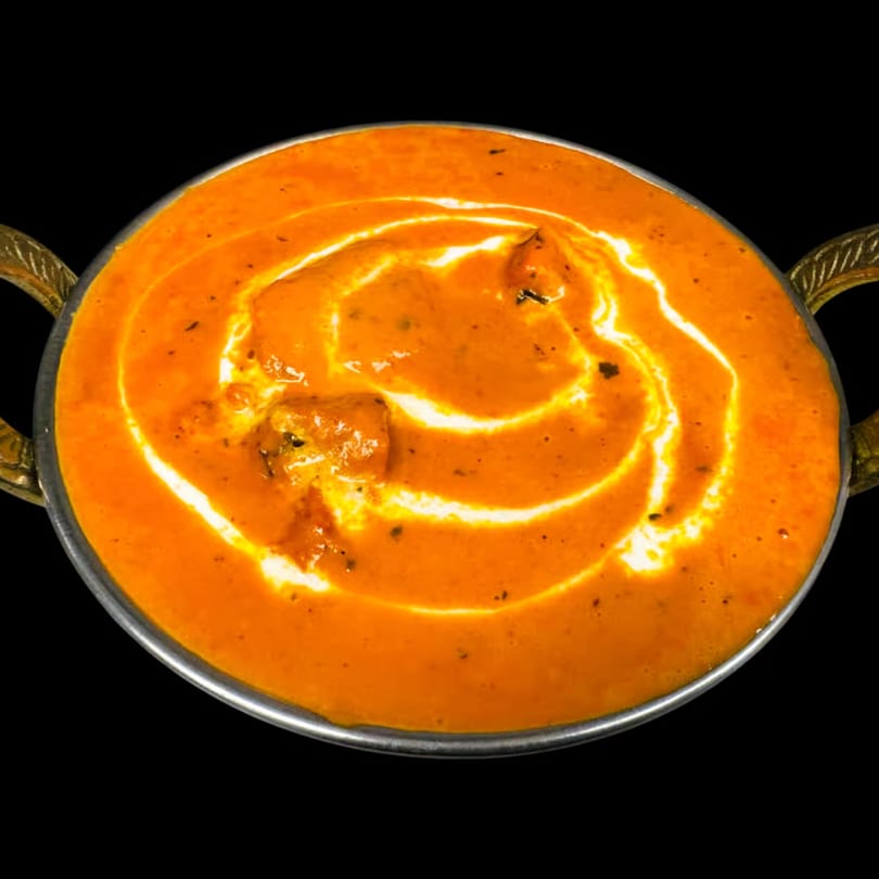 Dhaba Kitchen's butter chicken, a rich orange curry with cream swirls, served in a brass karahi.