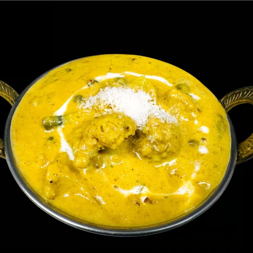 Dhaba Kitchen's Indian curry, a vibrant yellow dish with white cream swirls and shredded coconut.